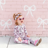 Child sitting on a pink brick wall with large white bows.
