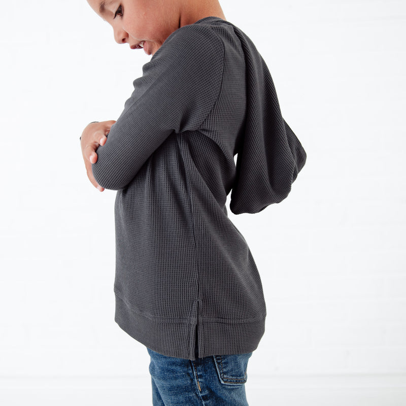 Side view of a dark grey waffle knit hoodie.