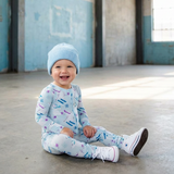 Baby sitting on a concrete floor in a large, open industrial space with high ceilings and large windows.