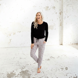 Woman in black top and patterned pants standing in a large, white, industrial-style room.