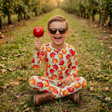 Child in a colorful outfit holding an apple in an orchard
