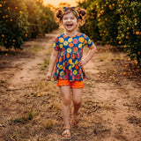 Young girl in a colorful dress walking through an orange grove at sunset.