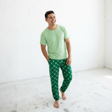 Man wearing a light green t-shirt and green patterned pants in a bright room.