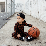 Child sitting on a sidewalk with a basketball, wearing a black and red outfit.