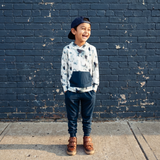 Child standing against a blue brick wall wearing a patterned shirt and jeans.