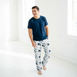 Man wearing a navy t-shirt and white floral pajama pants in a bright room.