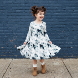 Young girl in a floral dress standing against a blue brick wall.