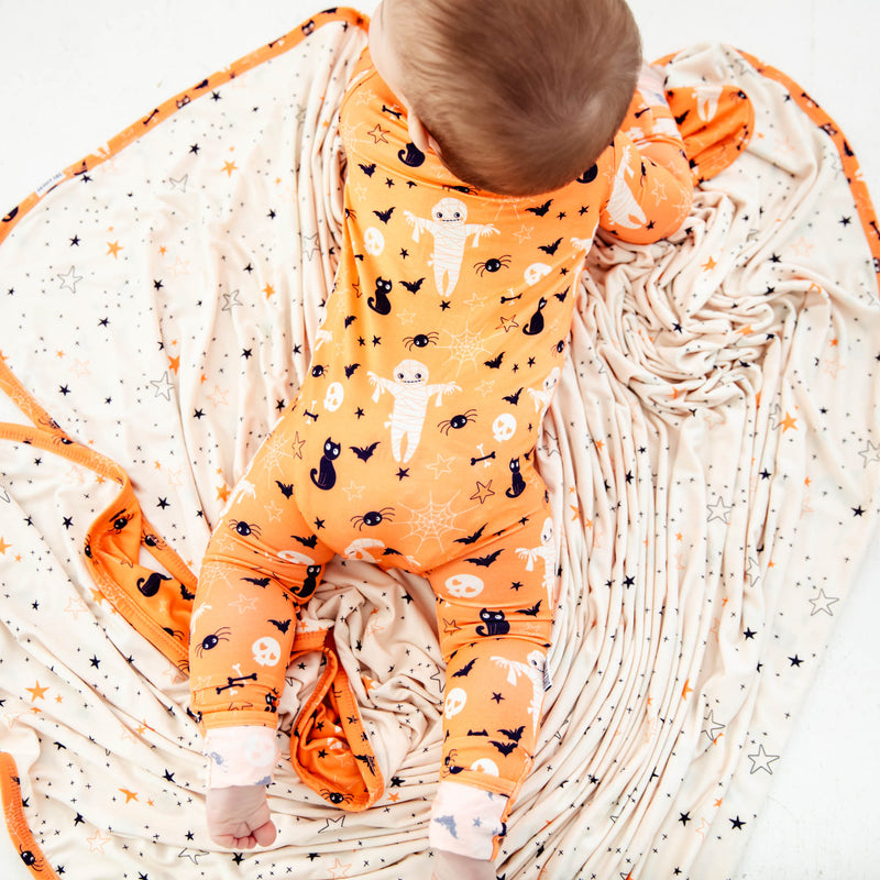 Baby in pjs laying on halloween blanket.