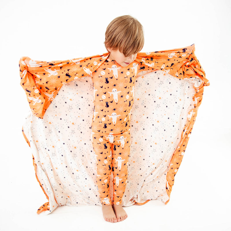Child in halloween pajamas with blanket over shoulders. 