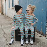 Two children in matching pajama sets sitting on a box against a blue wall.