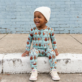 Child wearing a patterned outfit sitting on a curb with a blue brick wall background