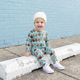 Child wearing a patterned outfit sitting on a curb against a light blue brick wall.