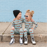 Two children in matching pajamas sitting on a sidewalk against a blue brick wall.