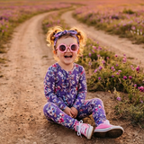 Child sitting on a dirt path in a field of flowers with a sunset in the background