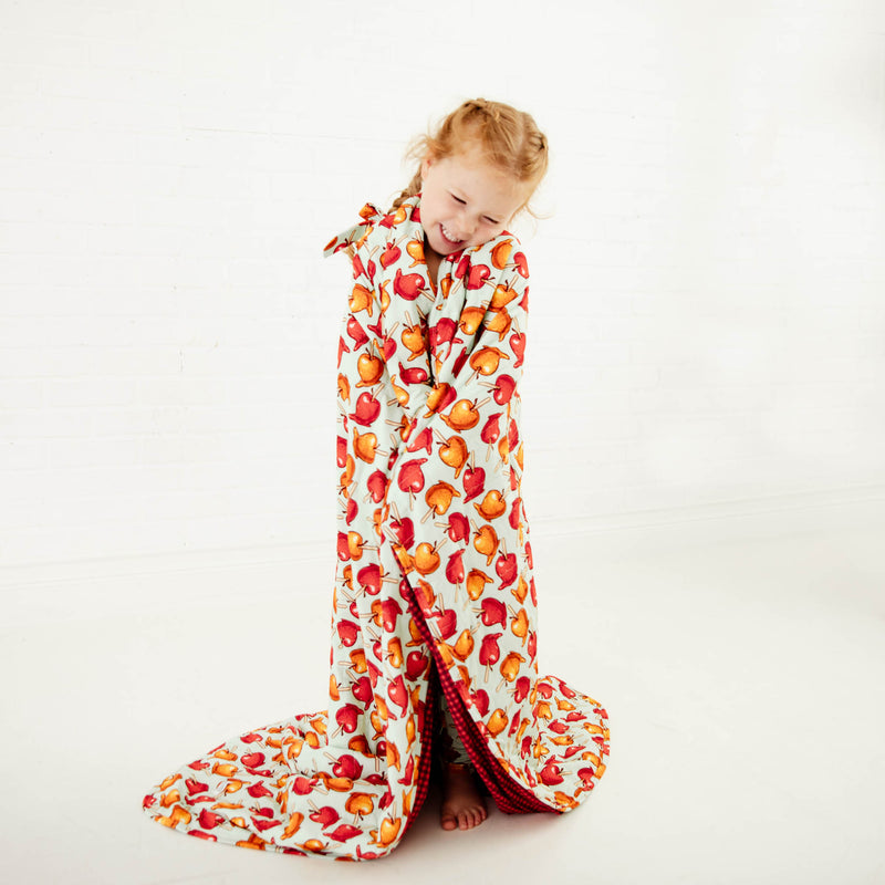 Child wrapped in blanket with caramel apple print. 