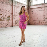 Woman in a pink dress standing in a large, sunlit room with pink brick walls.