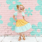 Child in a colorful dress standing in front of a pink brick wall with floral designs